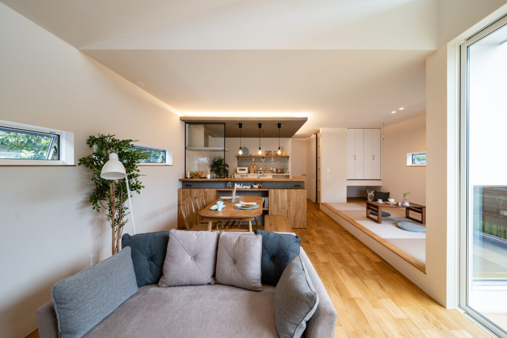 奥にキッチンがあり、ダイニングとソファー、右手には小上がりの和室がある平屋のリビング。