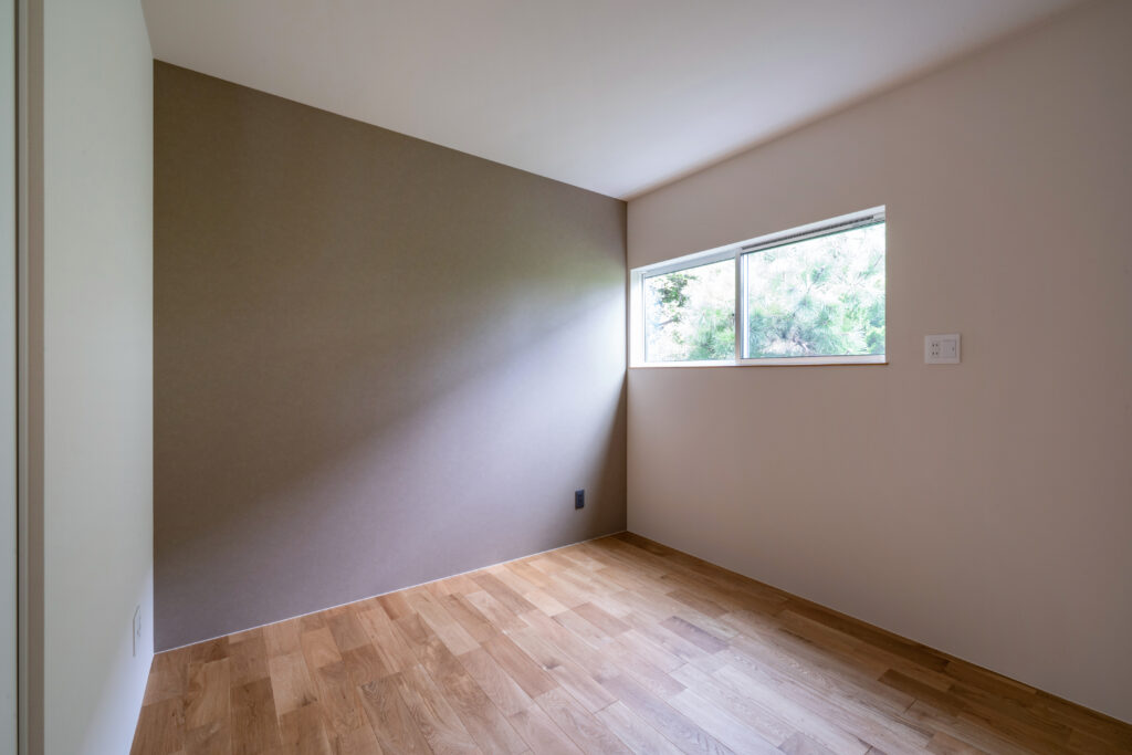 少し高めの位置にあるサイズの絞られた窓。明るい寝室。